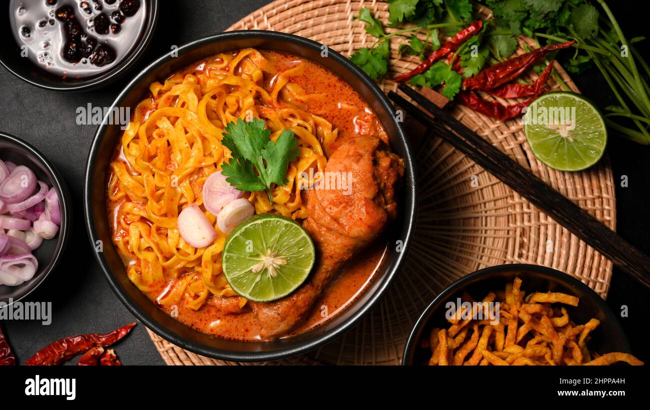 Draufsicht, Khao Soi Kai, cremig-würzige gelbe Kerrsuppe mit Hühnerdrumstick, serviert mit asiatischer Beilage. Nordthailändisches Speisekonzept Stockfoto