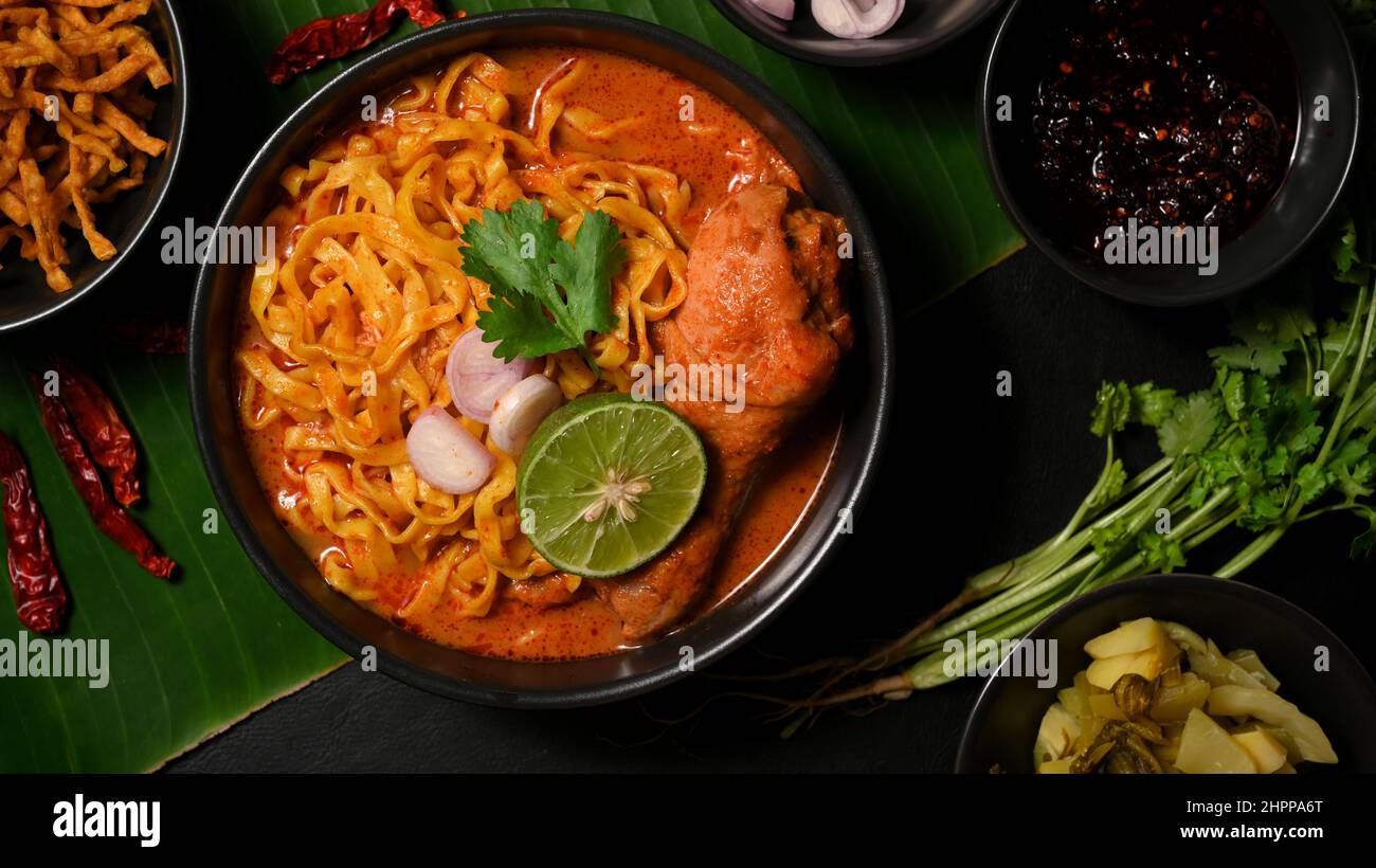 Draufsicht auf einen leckeren Khao Soi Kai in einer schwarzen Schüssel mit frischem Gemüse auf Bananenblatt Hintergrund. Nordthailändisches Speisekonzept. Stockfoto
