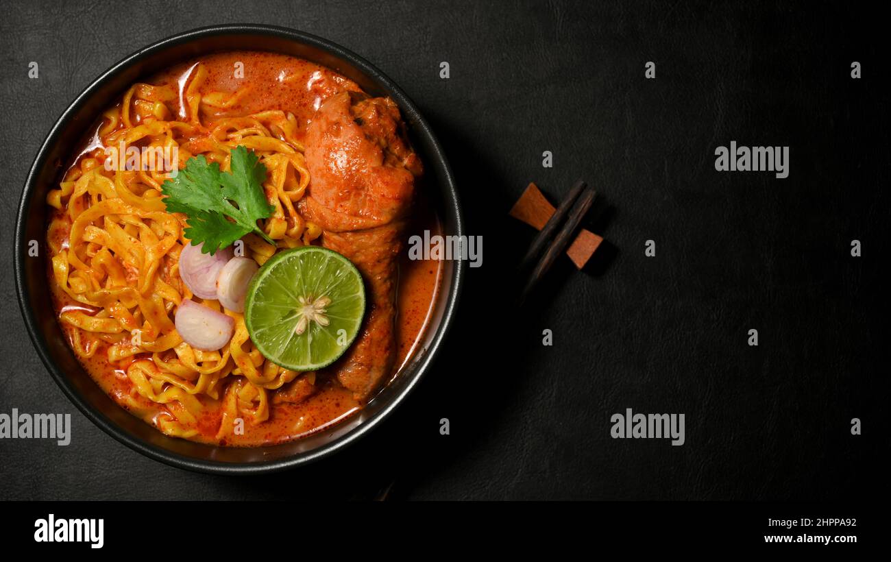 Overhead Shot, Khao Soi Kai oder Hühnerfleisch-Kerri mit Gewürzen und Eiernudeln auf schwarzem Hintergrund. Nordthailändisches Speisekonzept Stockfoto