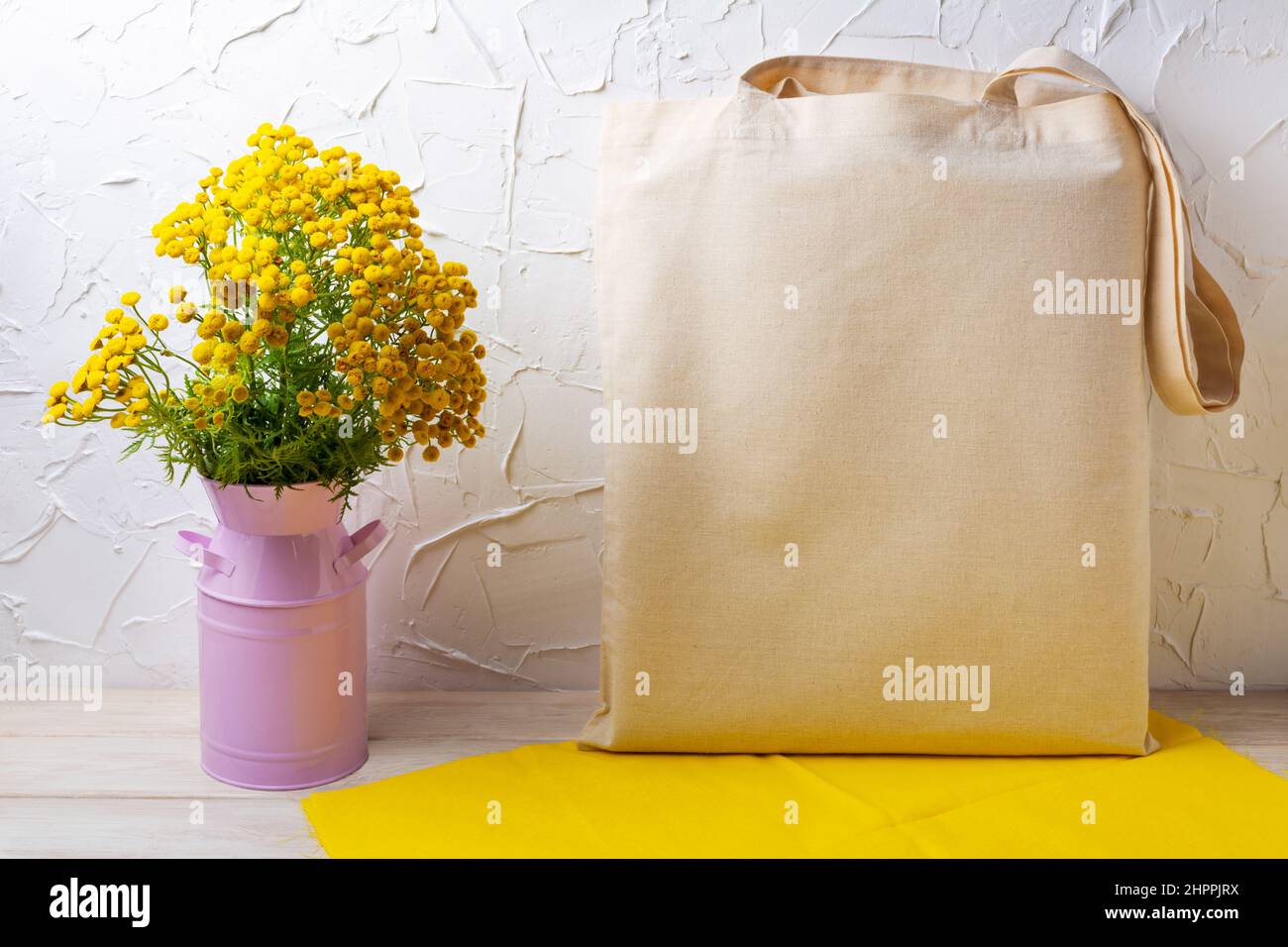 Canvas-Tragetasche Mockup mit wildgelben Blüten in der rosa Dose und Serviette. Rustikale Einkaufstasche aus Leinen für Branding-Präsentation Stockfoto