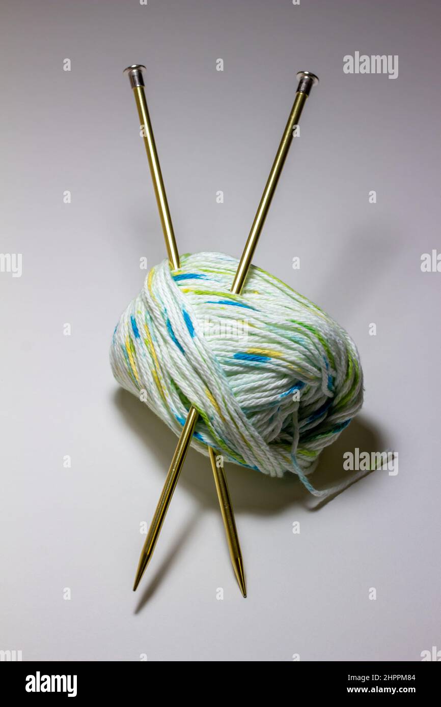 Nahaufnahme eines kleinen Skein aus weißem, blauem und grünem Baumwollgarn und einem Paar Stricknadeln aus Metall Stockfoto
