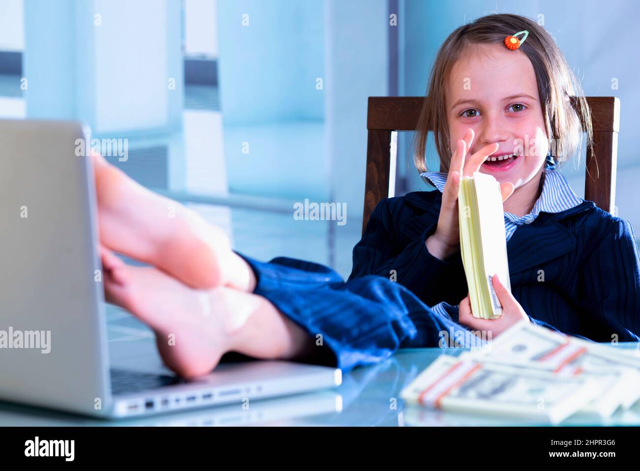 Geld ist der beste Motivator für die Arbeit. Porträt eines glücklichen lächelnden jungen, schönen Geschäftsmädchens, das die Füße auf einen Tisch legte und Stapel von US Dolla schnuppert Stockfoto