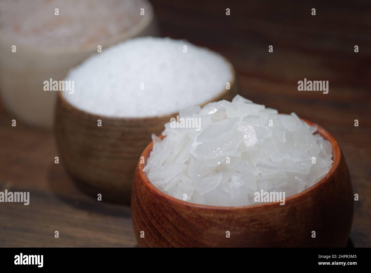 Verschiedene natürliche Salzsorten auf einem hölzernen Hintergrund. Salzkristalle in einem Holzbehälter Stockfoto