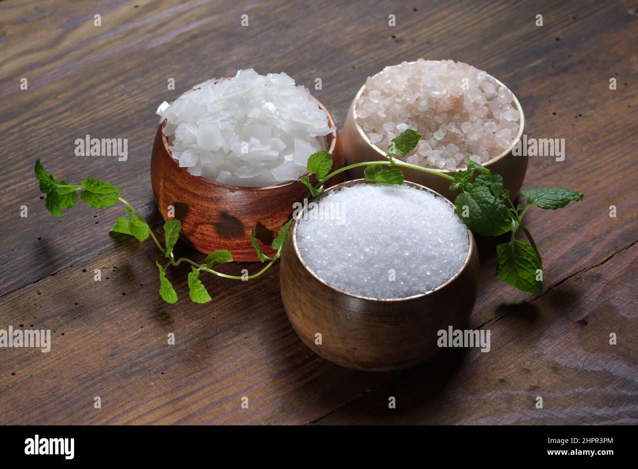 Verschiedene natürliche Salzsorten auf einem hölzernen Hintergrund. Salzkristalle in einem Holzbehälter Stockfoto