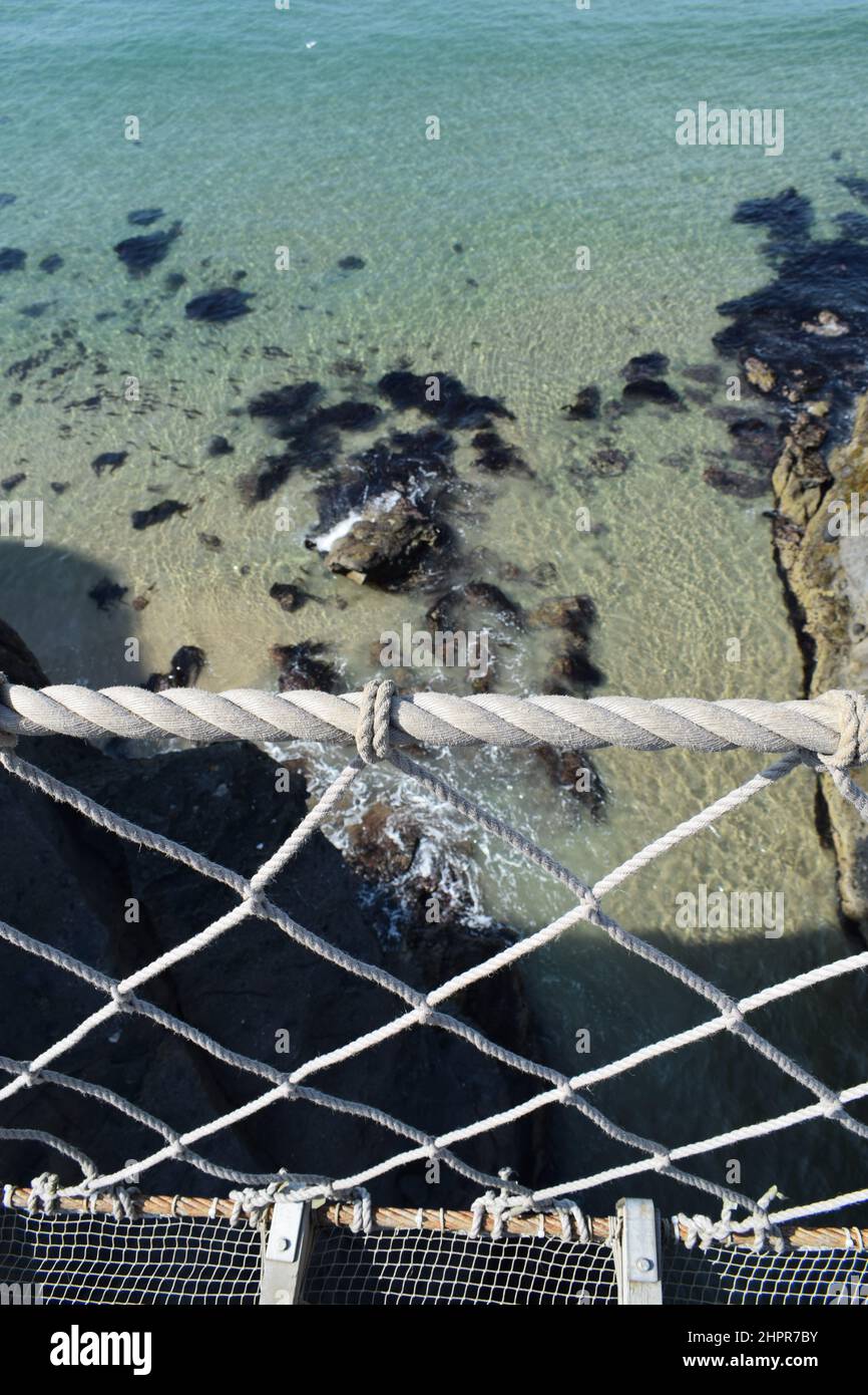 Carrick-a-Rede Seilbrücke aus nächster Nähe auf sauberem Wasser. Sandiger Meeresboden. Seilgeländer. Nordirland. Stockfoto