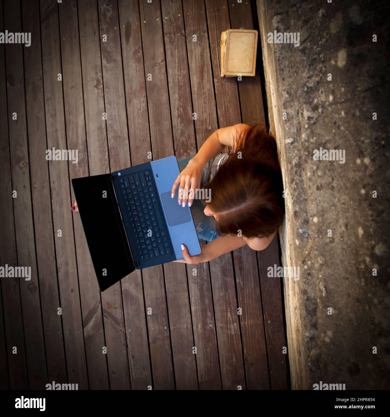 Draufsicht auf die schöne junge Geschäftsfrau, die freiberuflich auf einem Laptop im Freien auf einem Holzboden tippt. Die besten Orte, an denen man in einer Stadt Remote arbeiten kann. Stockfoto