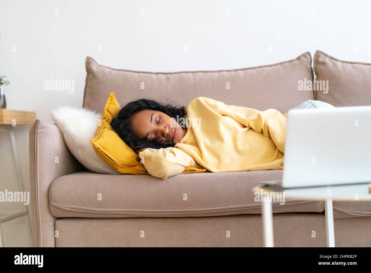 Gelangweilte afroamerikanische Frau schläft im Wohnzimmer auf der Couch, während sie einen Film auf dem Laptop spielt Stockfoto