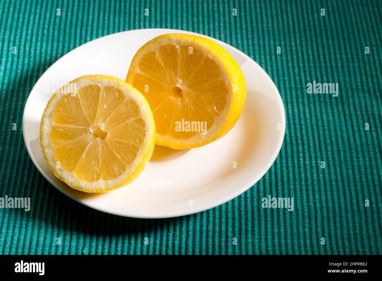 Eine saftige Zitrone, die auf einem Teller auf einem grünen Textilhintergrund auseinander geschnitten wurde, Platz für Text-Layout Stockfoto