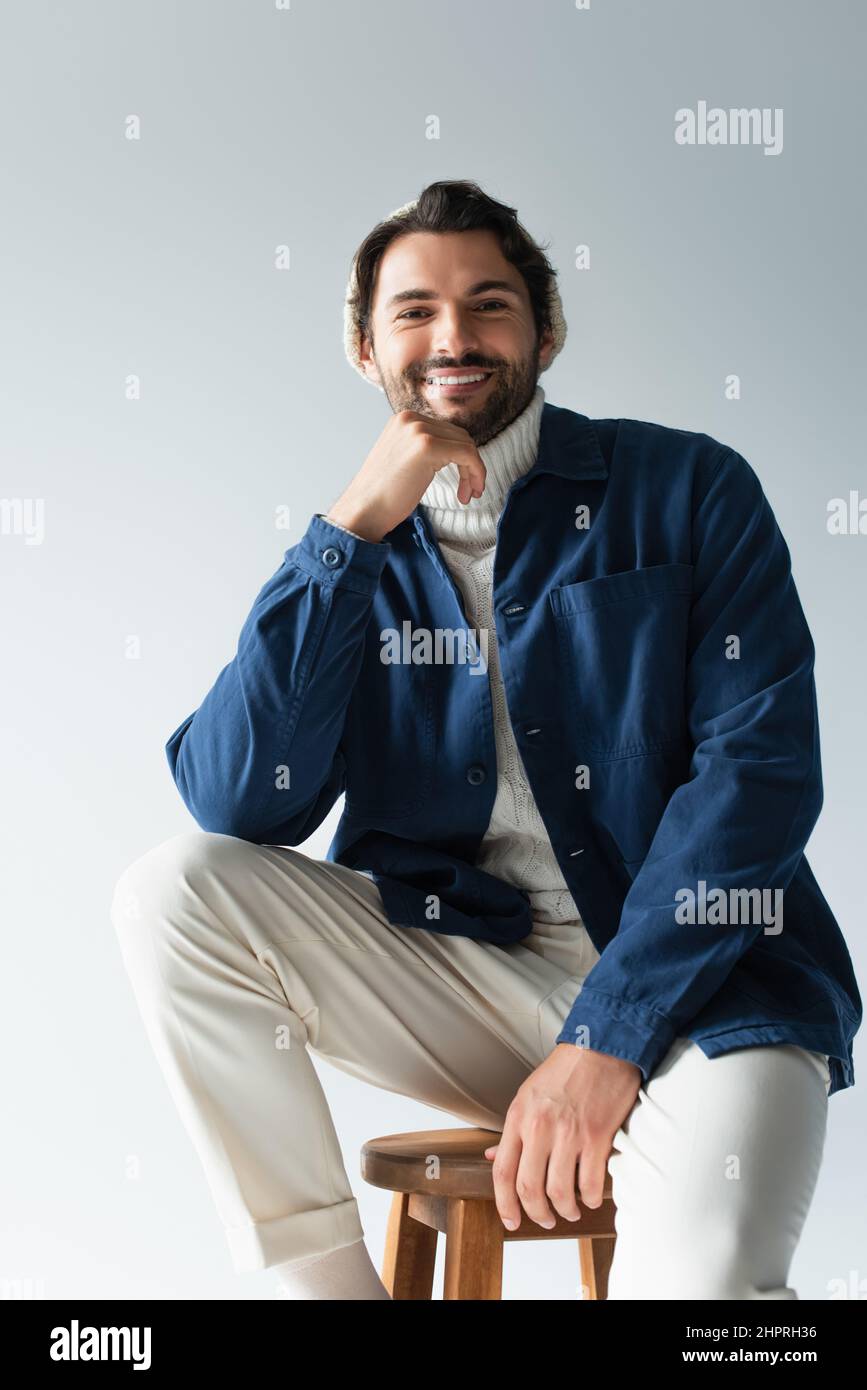 Fröhlicher Mann in weißer Hose und blauer Jacke, der die Kamera isoliert auf Grau ansieht Stockfoto