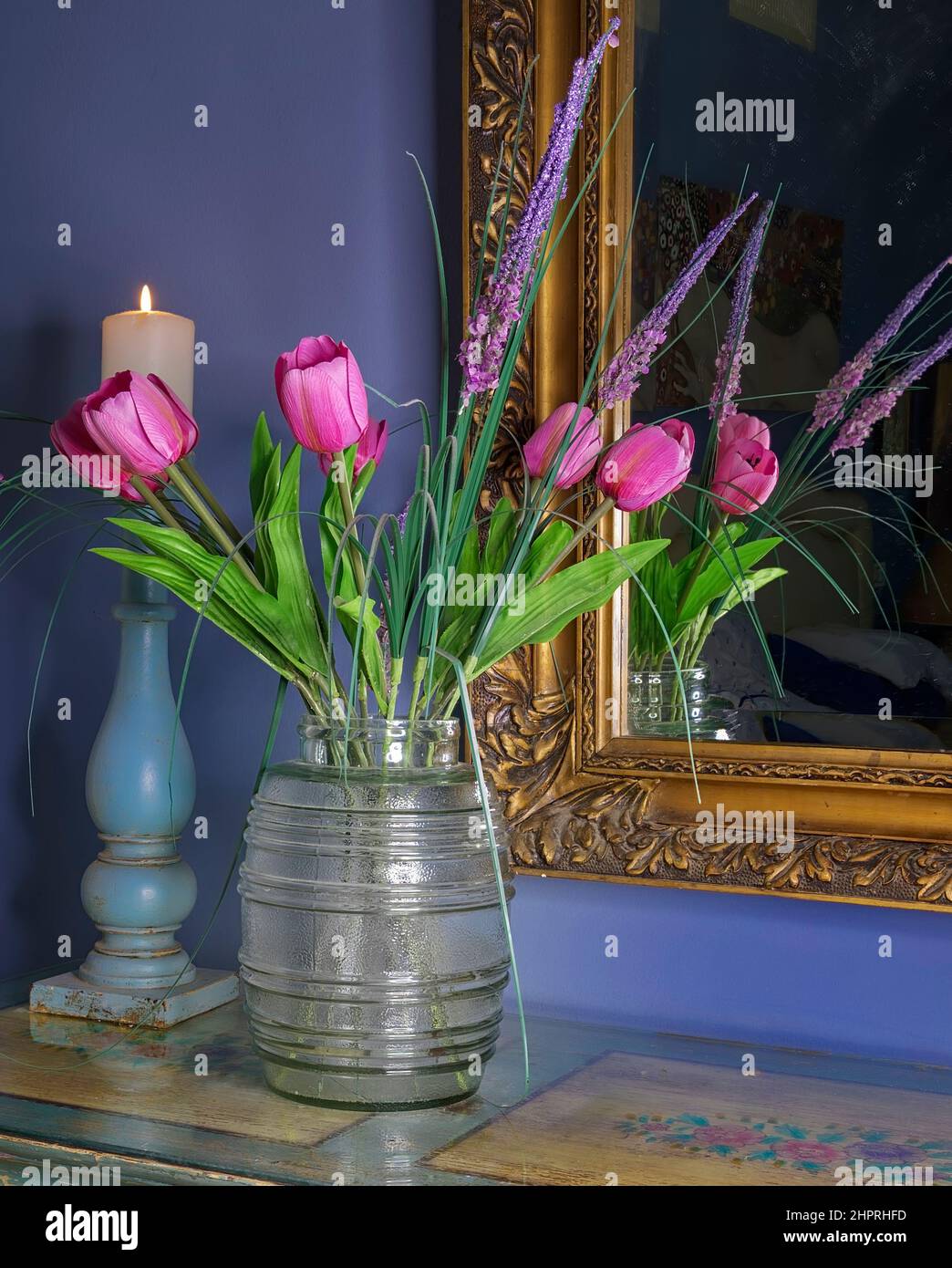 Rosa Tulpen . Fake Blumen in einer Vase mit antikem Gold umrandeten Spiegel und brennende Kerze im Kerzenhalter im Hintergrund. Stockbild Stockfoto