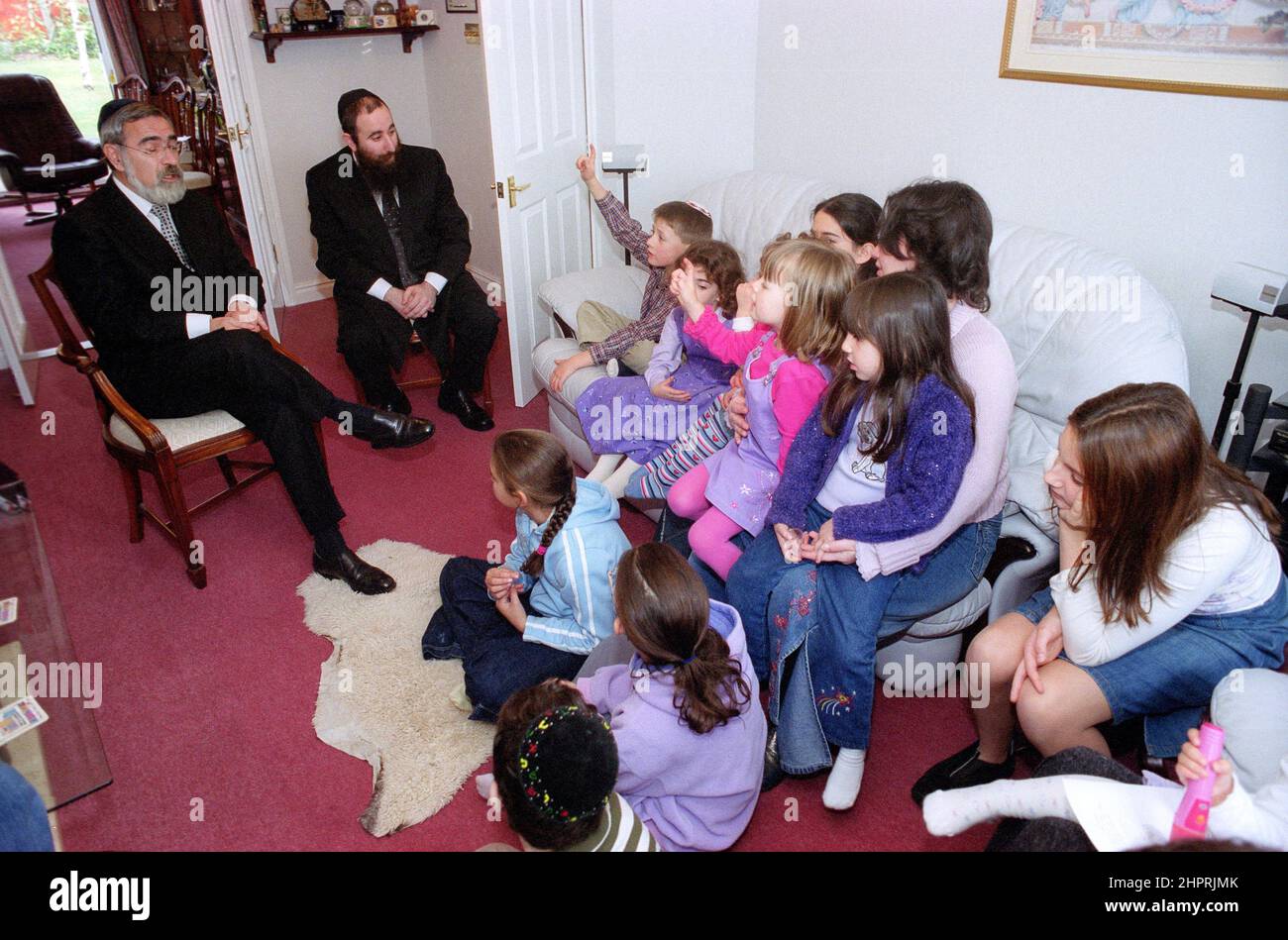 Der Oberrabbiner Jonathan Sacks war Ehrengast bei der Feier des 25th. Jahrestages der hebräischen Kongregation Solihull. Bei seinem Besuch traf er Kinder im Salon einer Familie aus der Gemeinde. Informell spricht er mit jungen jüdischen Kindern über ihre Arbeit im Cheder (Klassenzimmer) der Synagoge, blickt Gemeindepfarr Rabbi Yehuda Pink hin. Er sprach während des Gottesdienstes am 27th. Oktober 2002.der Bürgermeister von Solihull Cllr. Kate Wild war dabei und erhielt einen Strauß von der Cheder-Schülerin, 13 Jahre alt, Zipporah Gershon Stockfoto