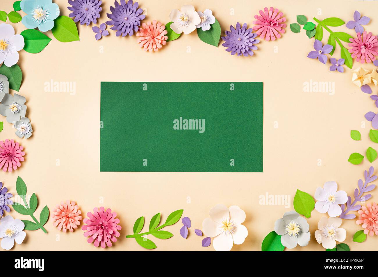 Flache Lage von floralen Hintergrund mit handgefertigten Papierblumen und grünen leeren Papierbogen. Papierkunst und Handarbeit. Draufsicht. Frühling oder Sommer Stockfoto