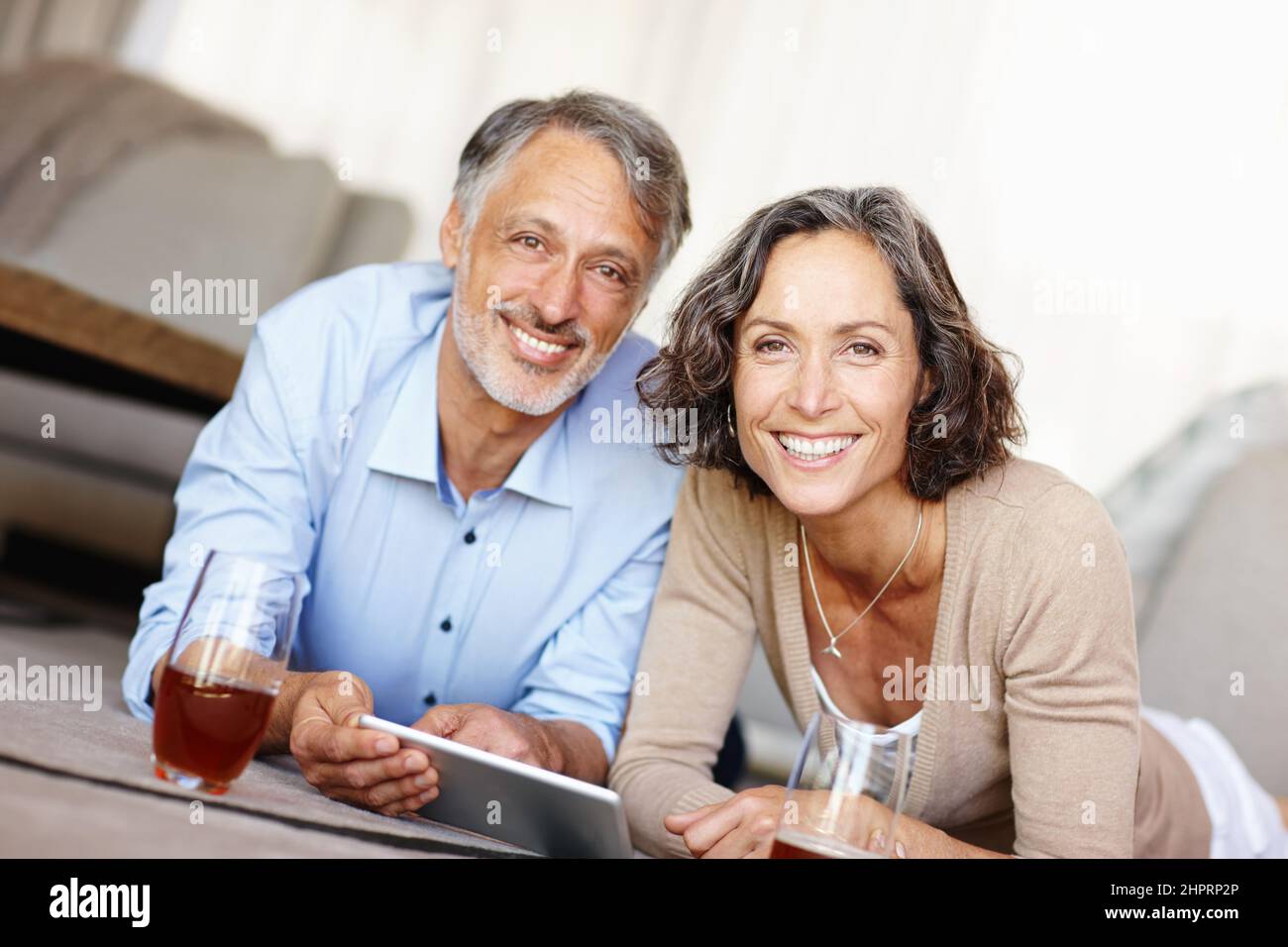 Spontaneität ist das Gewürz des Lebens. Porträt eines glücklichen, reifen Paares, das auf dem Boden liegt und ein digitales Tablet nutzt. Stockfoto