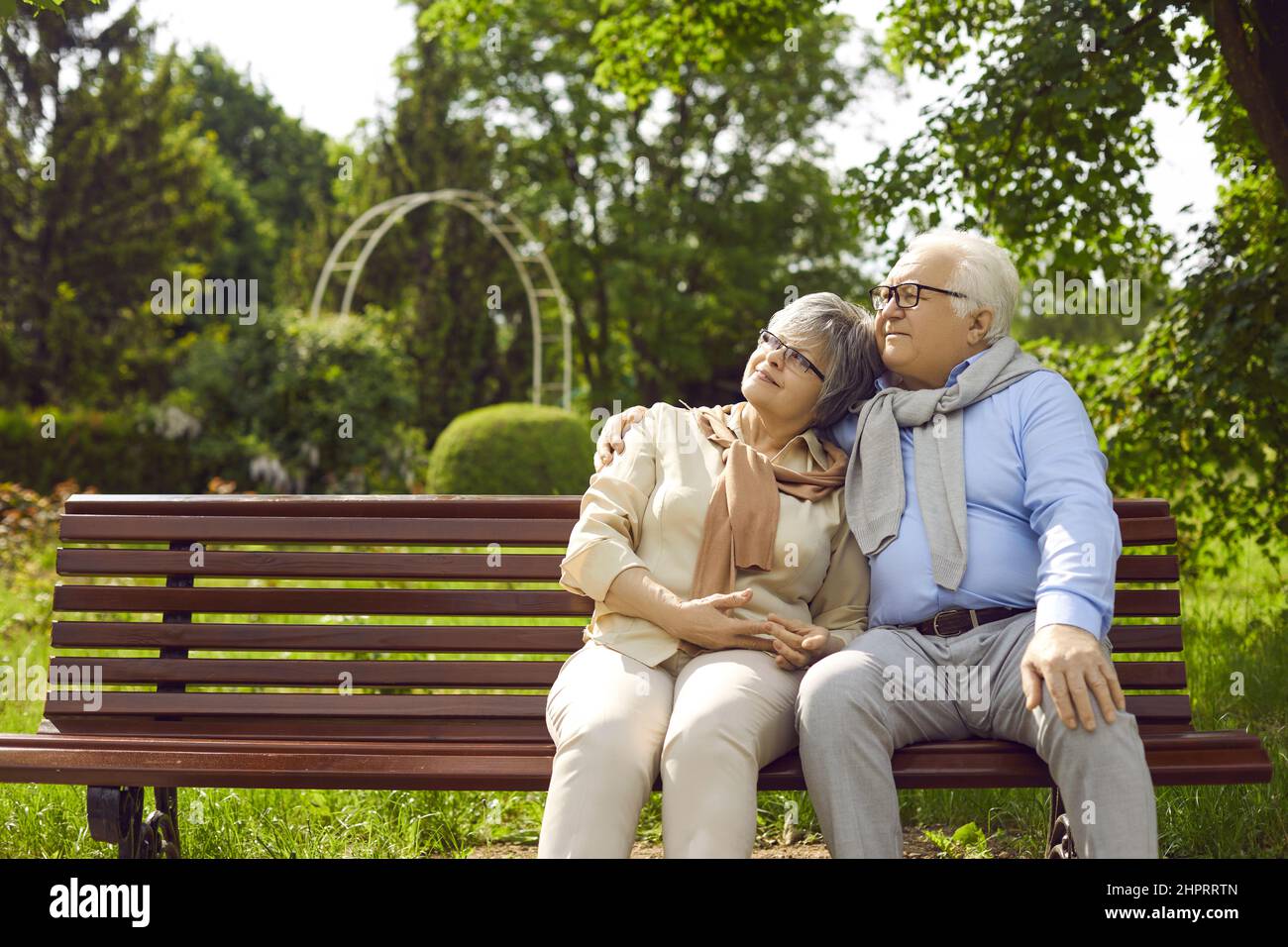 Ein romantisches, liebevolles Senioren-Paar, das auf der Bank sitzt und sich im Park umarmt Stockfoto