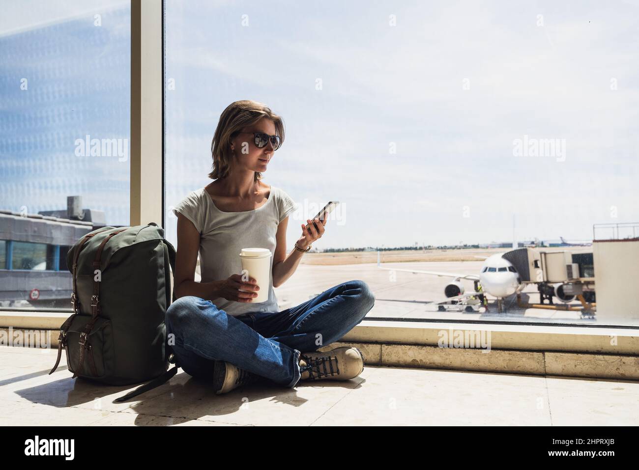 Junge Frau am Flughafen, mit Smartphone und Kaffee trinken, Reisen, Urlaub und aktiven Lifestyle-Konzept Stockfoto
