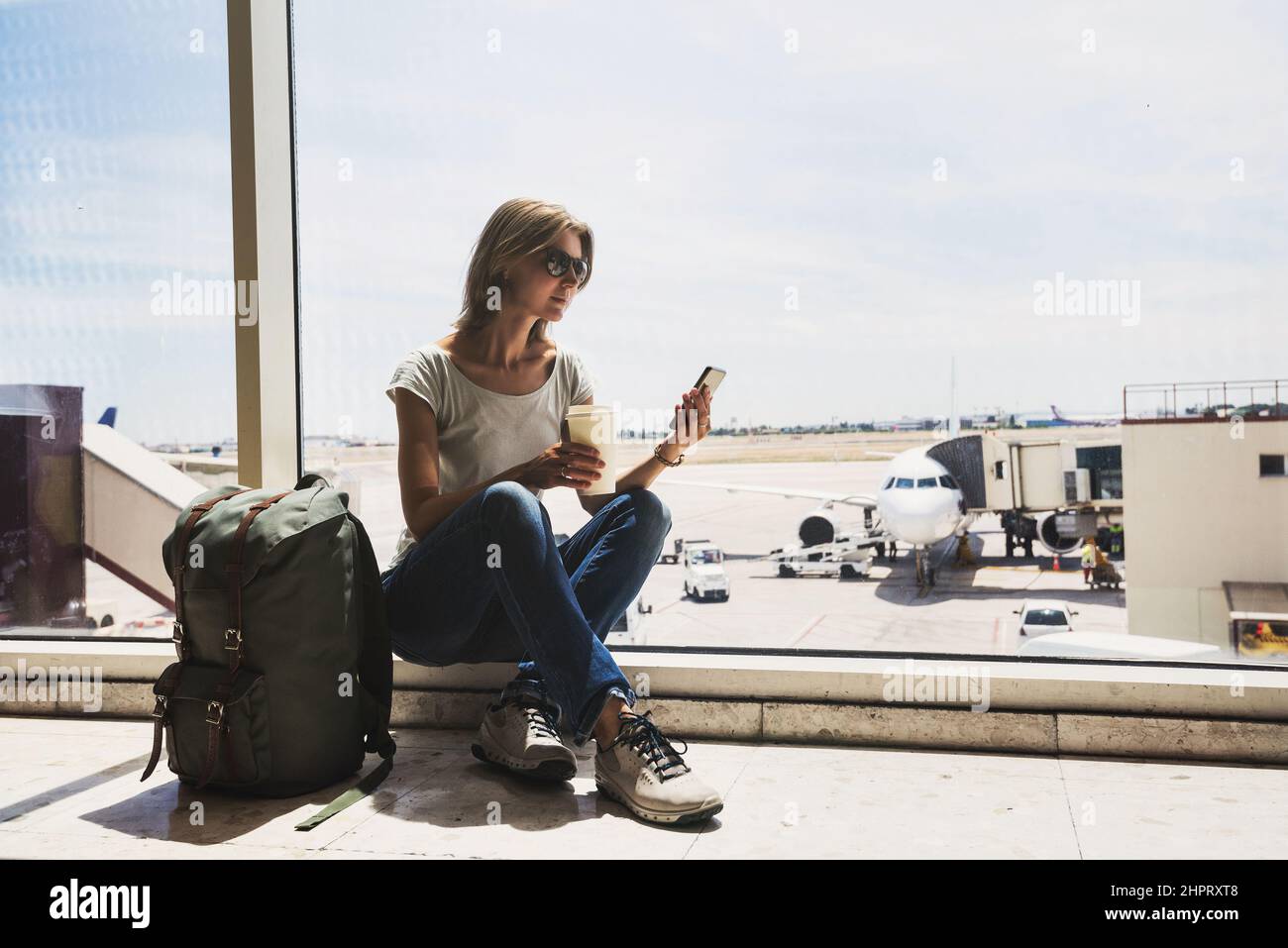 Junge Frau am Flughafen, mit Smartphone und Kaffee trinken, Reisen, Urlaub und aktiven Lifestyle-Konzept Stockfoto