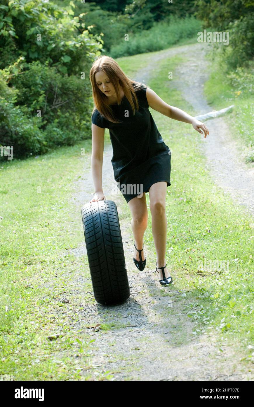 Junge Frau schob einen Autoreifen den Hügel hinunter Stockfoto