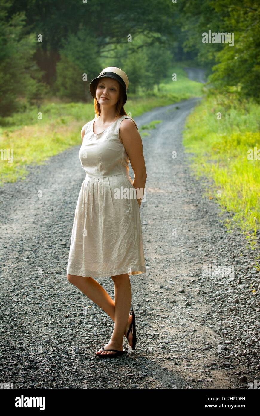Junge Frau, die auf einer Schotterstraße steht, Hände hinter ihrem Rücken Stockfoto
