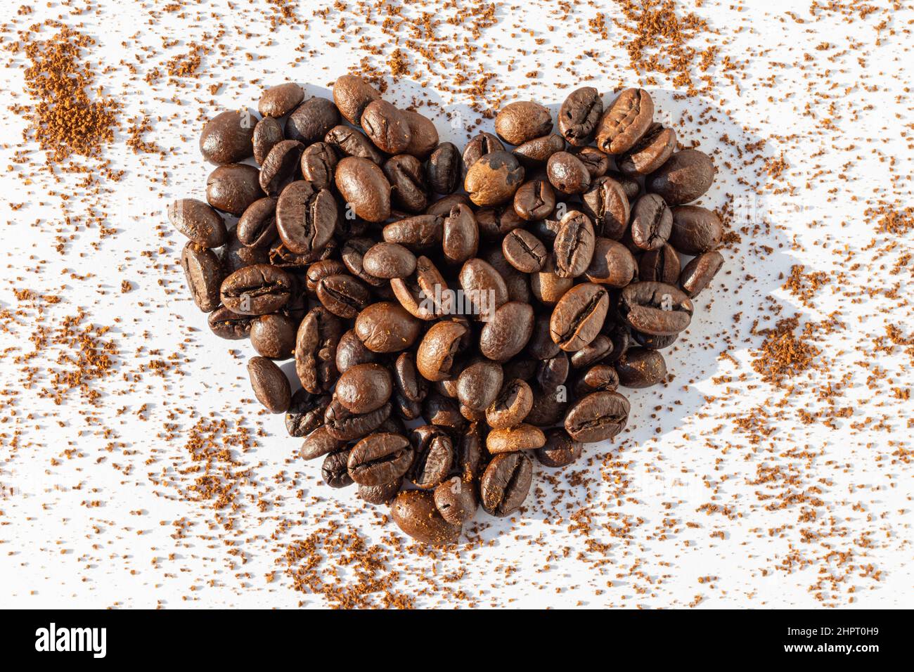 Herzform aus braunen gerösteten Kaffeebohnen Robusta, Arabica-Kaffee auf einem Hintergrund aus gemahlenem Kaffee auf weißem Hintergrund. Stockfoto