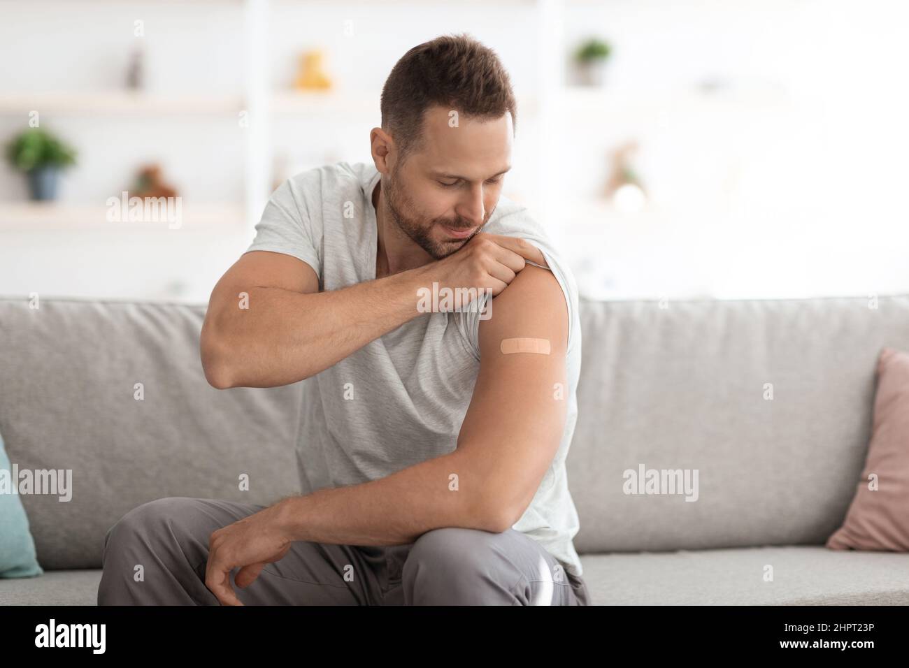 Covid-19-Impfung. Junger, fröhlicher Kaukasier, der nach der Impfung die Schulter mit medizinischem Gips zeigt, leerer Raum Stockfoto