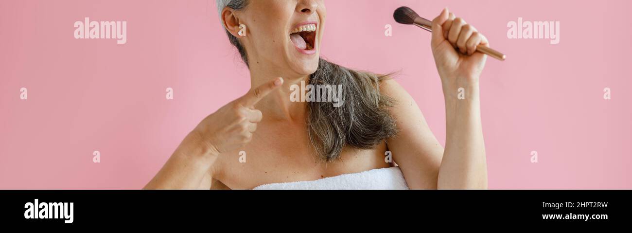 Aufgeregt mittleren Alters asiatische Modell mit Frottee Handtuch gewickelt singt auf rosa Hintergrund Stockfoto