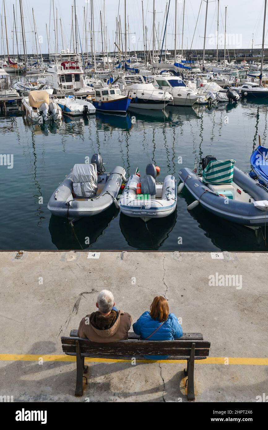 Blick von einem Paar, das an einem sonnigen Wintertag auf einer Bank am Ufer des Alten Hafens von Sanremo sitzt, in Imperia, Ligurien, Italien Stockfoto