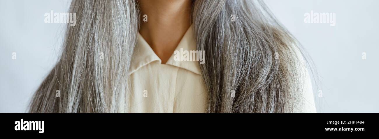 Frau mittleren Alters mit langen silbernen Haaren lächelt auf hellgrauem Hintergrund Stockfoto