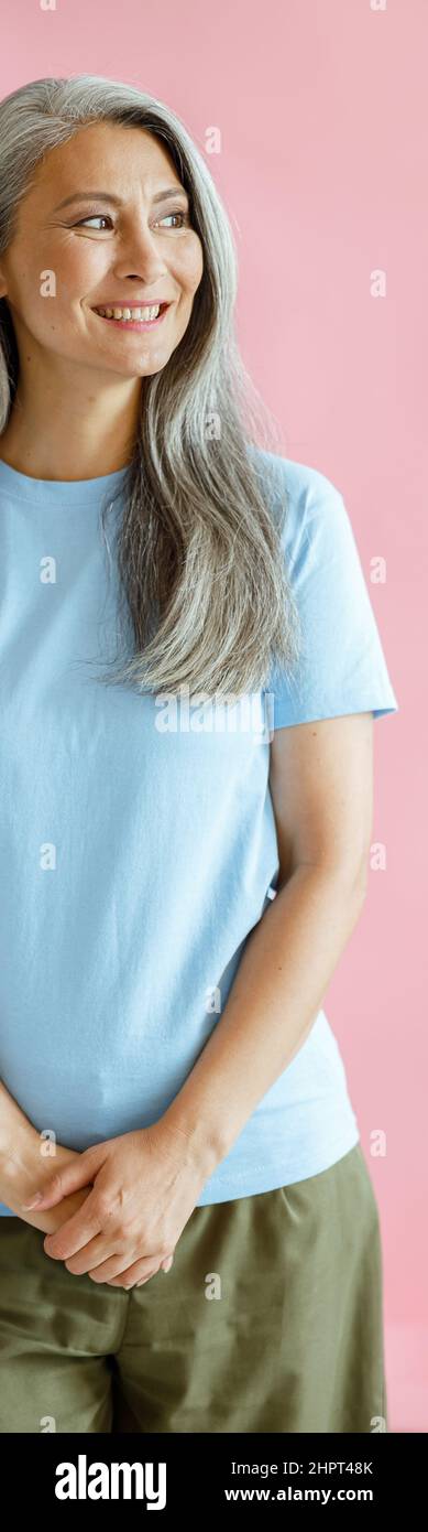 Glückliche silberhaarige asiatische Frau mittleren Alters in T-Shirt steht auf rosa Hintergrund Stockfoto