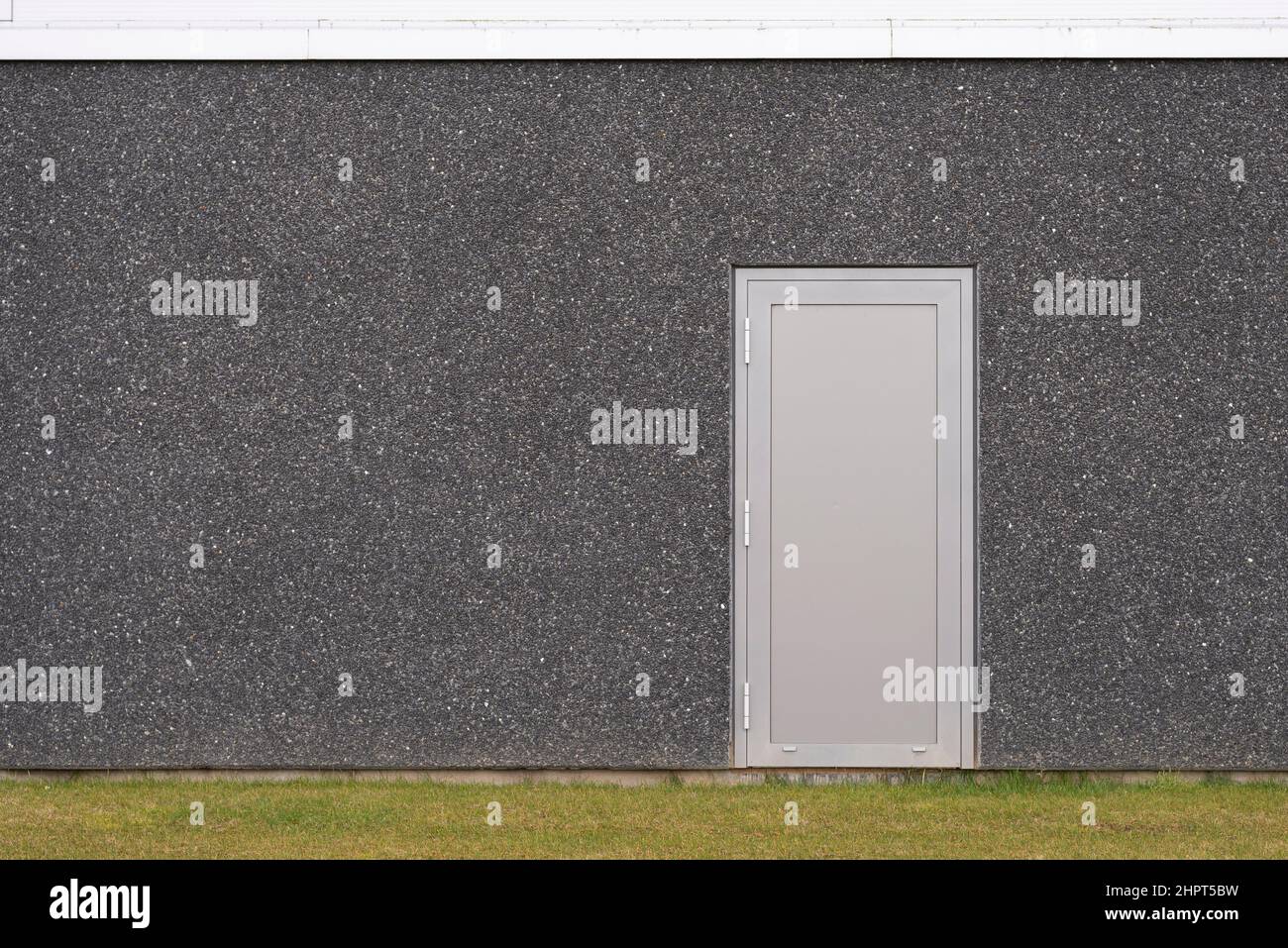Eine graue Sicherheitstür auf einem dunkelgrauen Betongebäude mit Rasen im Vordergrund, Frederikssund, Dänemark, 22. Februar 2022 Stockfoto
