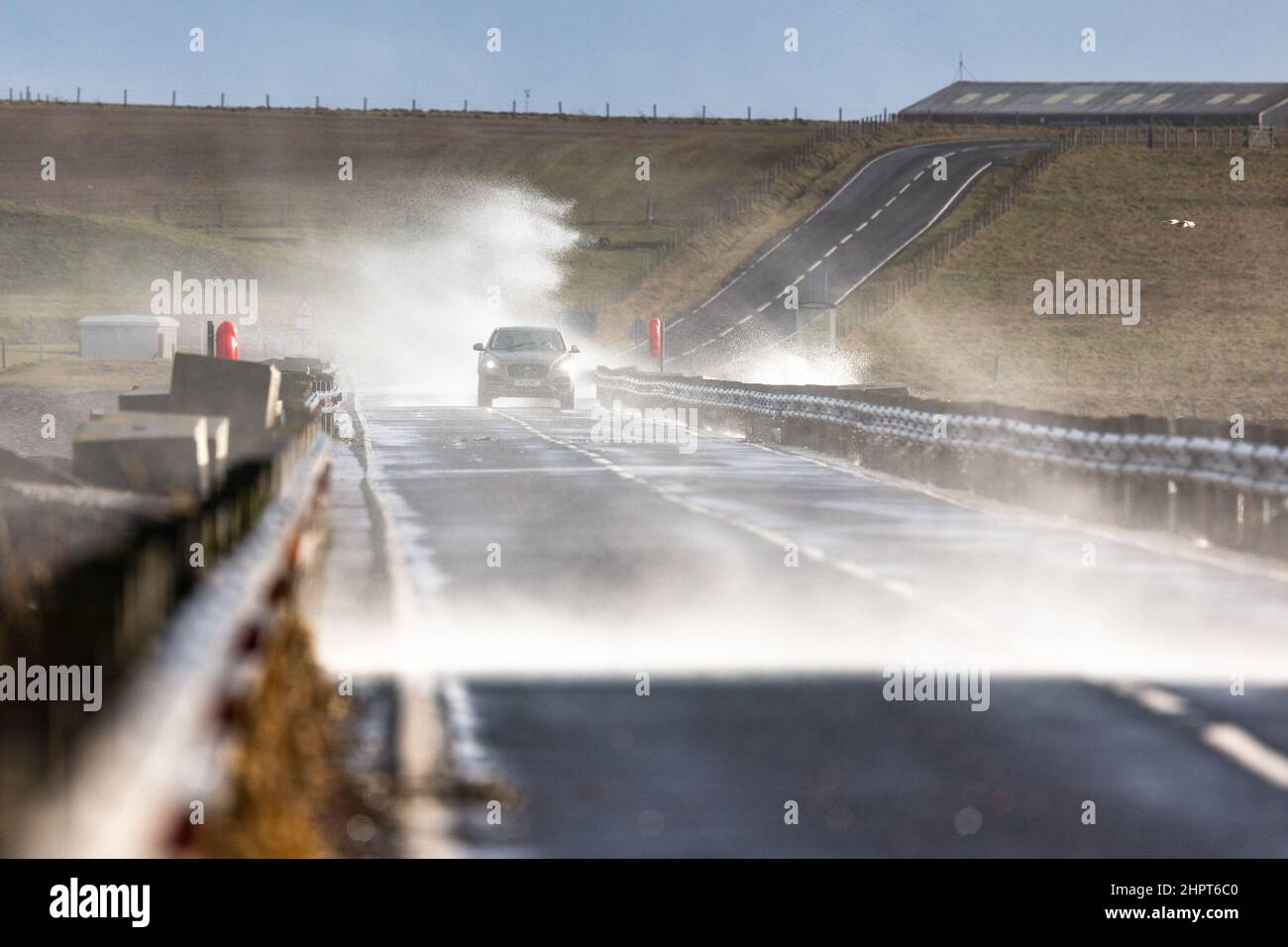 Orkney Islands, Schottland, Großbritannien. 23rd. Februar 2022. Starke Winde bringen dramatische Wellen und sprühen über den Verkehr, der die berühmte Churchill Barrier auf den Orkney Islands überquert. Die Barrieren - die von italienischen Kriegsgefangenen während des letzten Krieges errichtet wurden - sind die einzigen Landverbindungen zwischen den südlichen Orkney-Inseln. Kredit: Peter Lopeman/Alamy Live Nachrichten Stockfoto