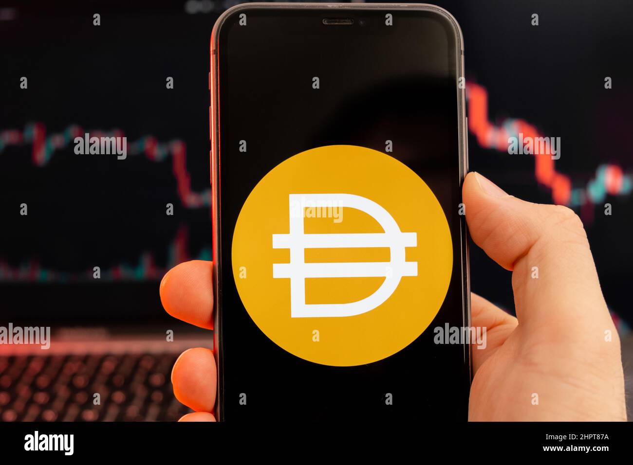 Dai DAI Kryptowährung Logo auf dem Bildschirm des Smartphones in mans Hand mit Abwärtstrend auf dem Chart auf rotem Hintergrund, Februar 2022, San Francisco, USA. Stockfoto