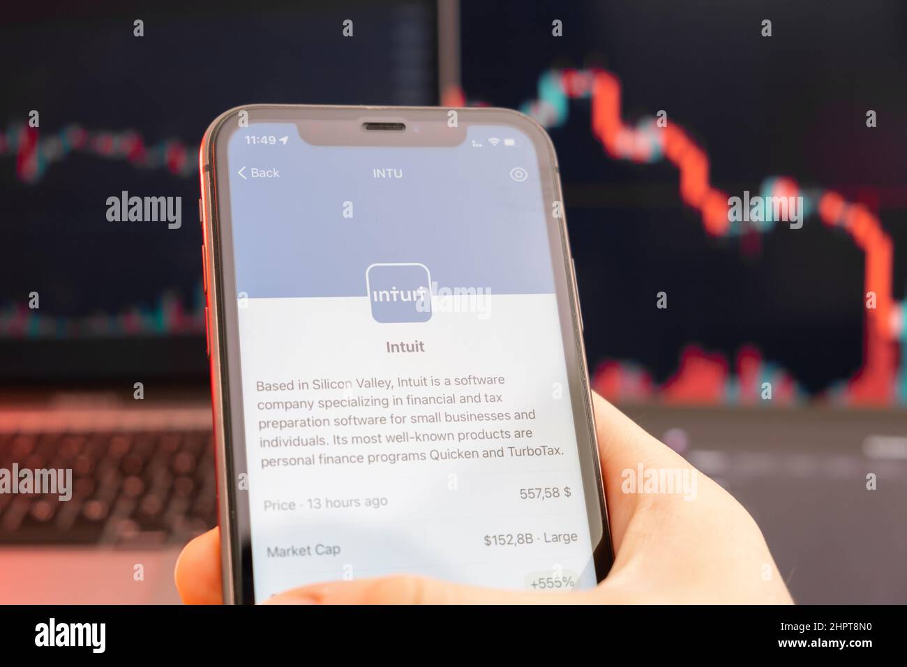 Der Abwärtstrend der Aktienkursen von Intuit mit roten Graphen im Hintergrund. Man hands Holding a Smartphone with Logo on the screen, February 2022, San Francisco, USA. Stockfoto