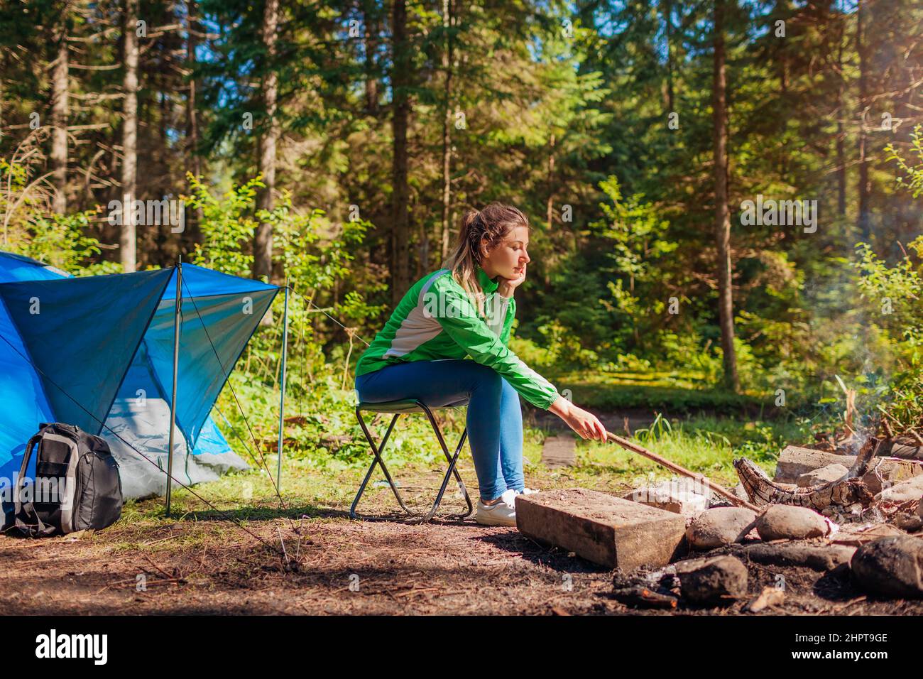 Frau, die sich am Lagerfeuer im Wald neben dem Zelt entspannt. Camping im Sommer. Allein reisen Stockfoto