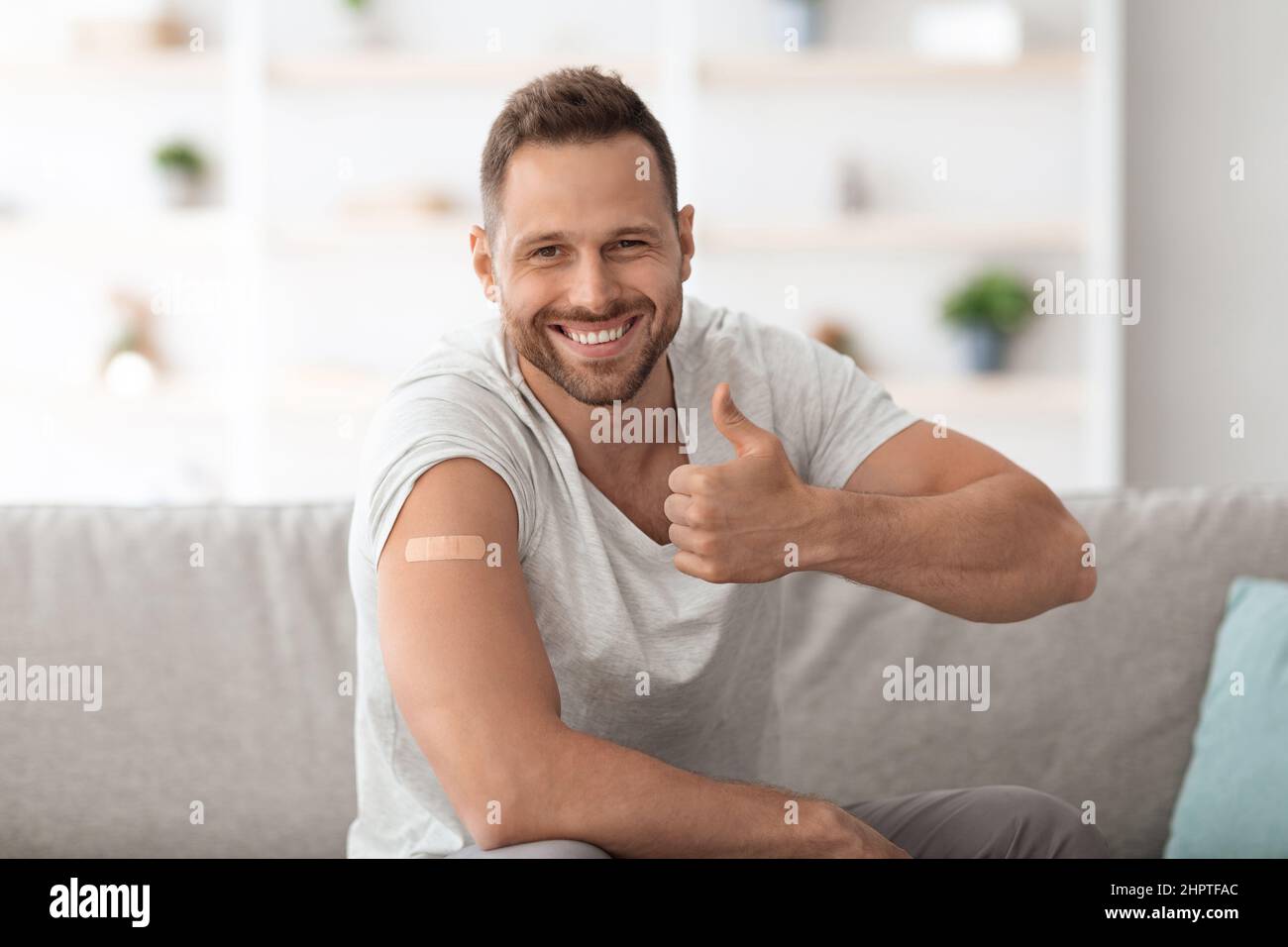 Glücklicher Kerl, der Impfungen genehmigt, nach der Injektion medizinischen Pflaster auf der Schulter zeigt und den Daumen nach oben zeigt, freien Platz Stockfoto