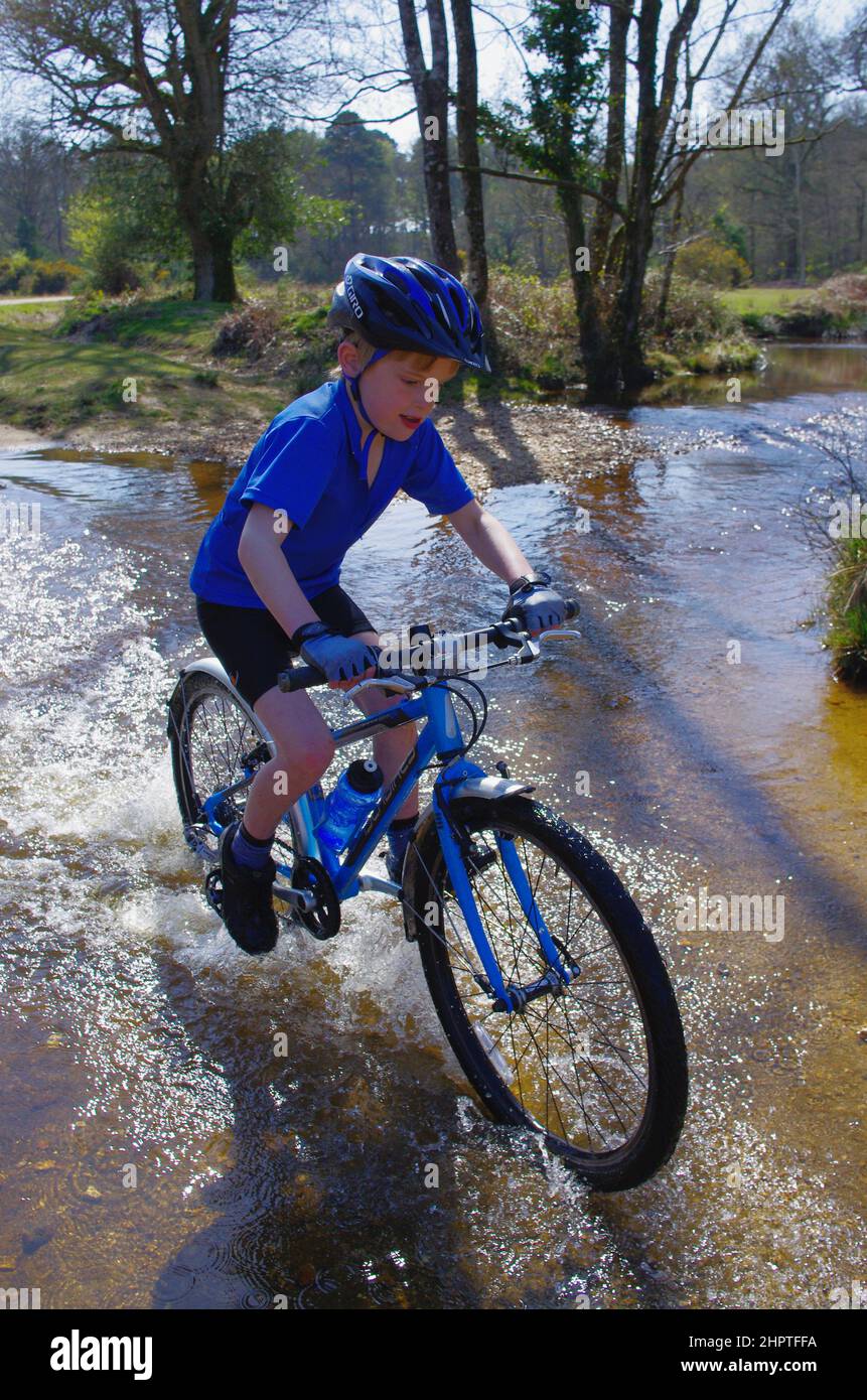 Ein Junge fährt selbstbewusst durch den Fletchers Water Ford im New Forest National Park, mit Spaß und Spritzwasser. Stockfoto