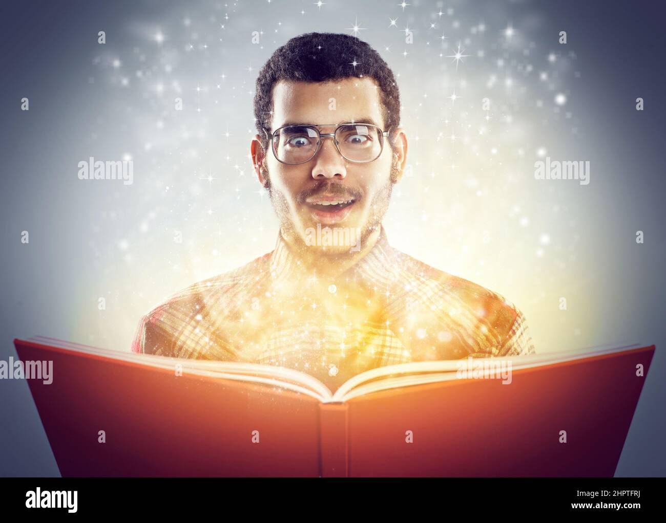 Verzaubert von seinen verborgenen Geschichten. Eine ausgeschnittene Aufnahme eines jungen Erwachsenen, der ein Buch mit leuchtenden Seiten liest. Stockfoto