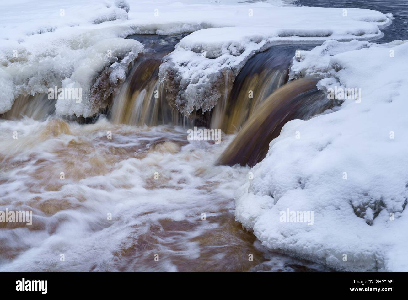 Eisfrei laufender Fluss im verschneiten Wald an einem düsteren kalten Wintertag Stockfoto