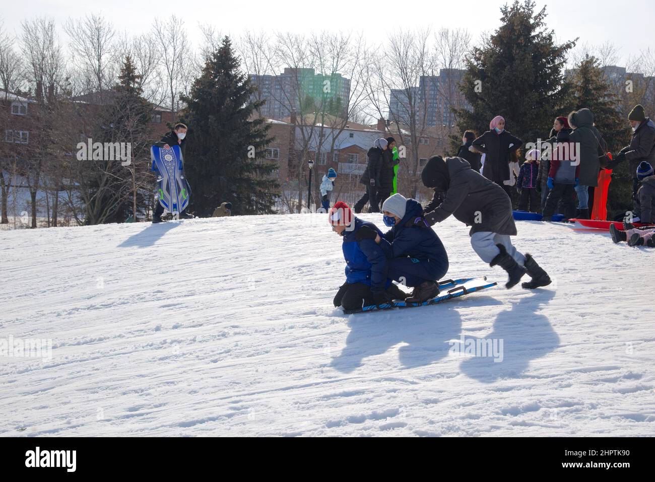 Toronto, Ontario / Canada - 02/21/2022: Familienaktivitäten unter COVID-19. Mutter und Kinder, die im Winter draußen Rodeln spielen. Stockfoto