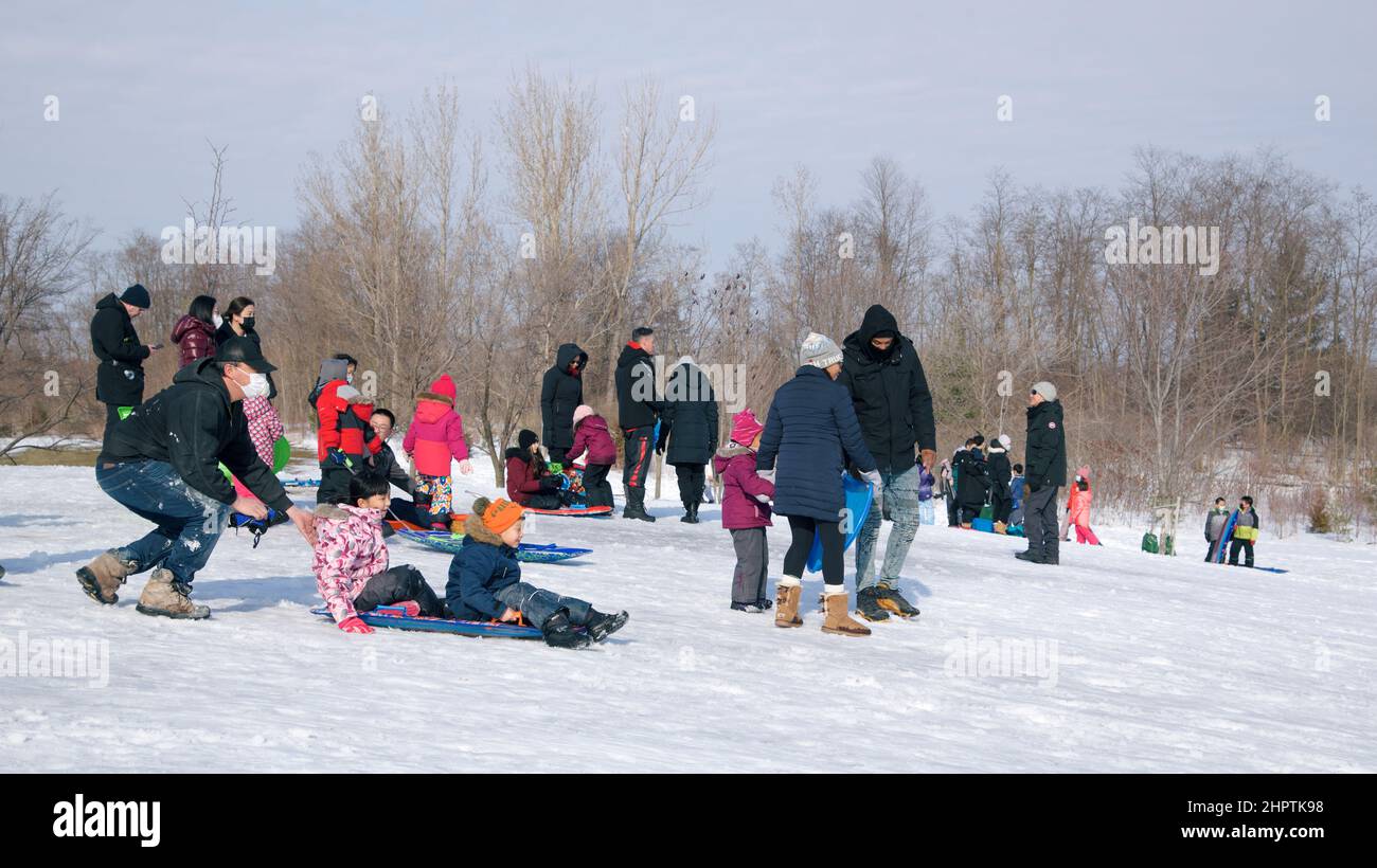 Toronto, Ontario / Canada - 02/21/2022: Familienaktivitäten unter COVID-19. Vater und Kinder spielen im Winter Rodel. Stockfoto