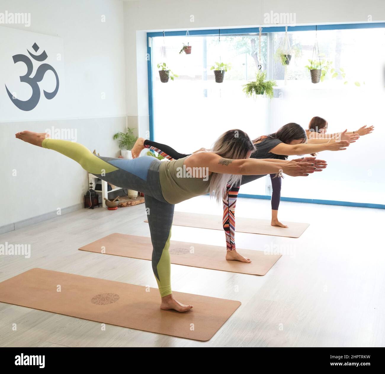 Drei attraktive junge Frauen, die Yoga praktizieren, stehen in der Warrior Three Übung in der Yogaklasse, Virabhadrasana III Haltung, Stockfoto