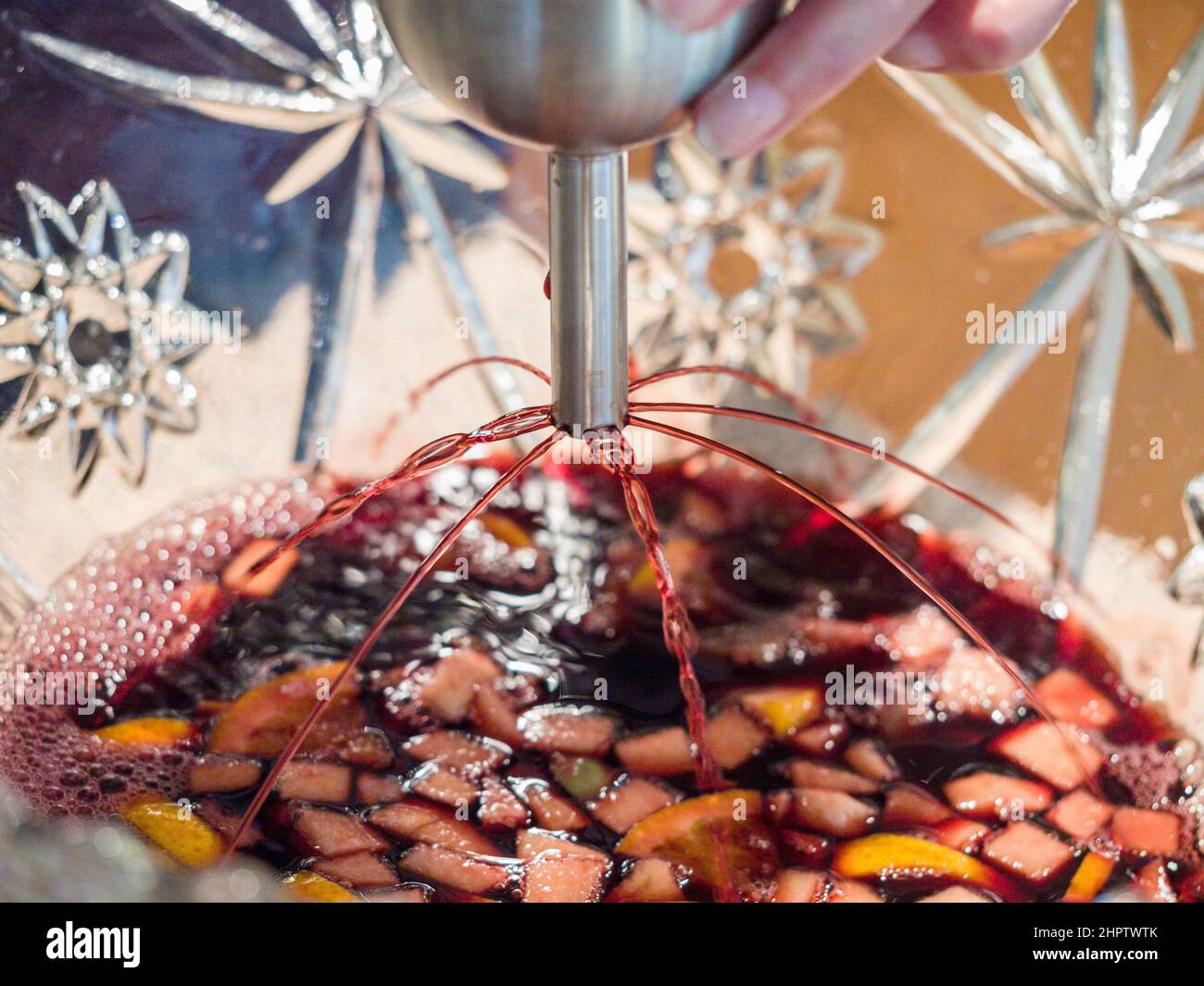 Rotwein mit Früchten durchlüften: Wein wird mit einem Belüfter mit mehreren Ausgiessen dekorativ in eine geschliffene Glaskaraffe verteilt. Obst schwimmt im Wein/Punsch unten. Stockfoto