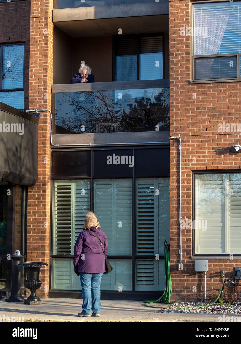 Fernbesuch während einer Pandemie-Sperre: Eine Frau besucht ihre Mutter, die während der COVID-19-Pandemie von 2020 und 2021 auf einem Balkon im zweiten Stock über ihr thront. Stockfoto