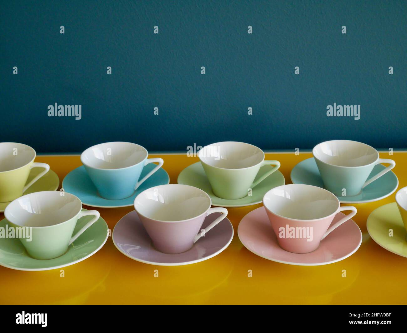 Reihe von Pastell-Kaffeebechern aus Vintage-Pastelltönen auf dem gelben Tisch vor Benzinhintergrund. Kaffeeparty am Nachmittag. Stockfoto