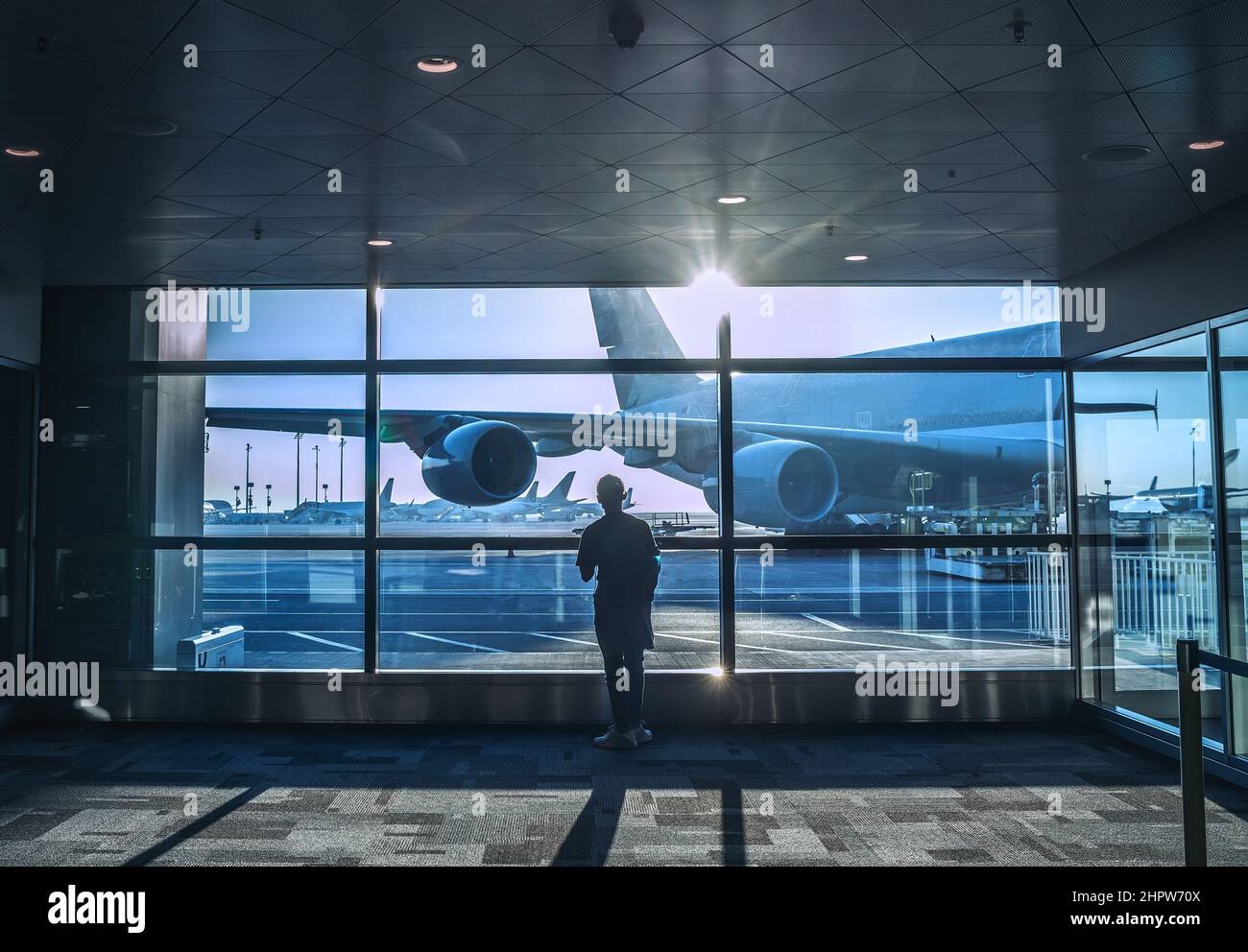 Allein Reisender Junge, der neben einem breiten Fenster im Flughafenterminal stand und auf das Einsteigen in einem Flugzeug wartete, das sich auf den Flug mit m vorbereitete Stockfoto