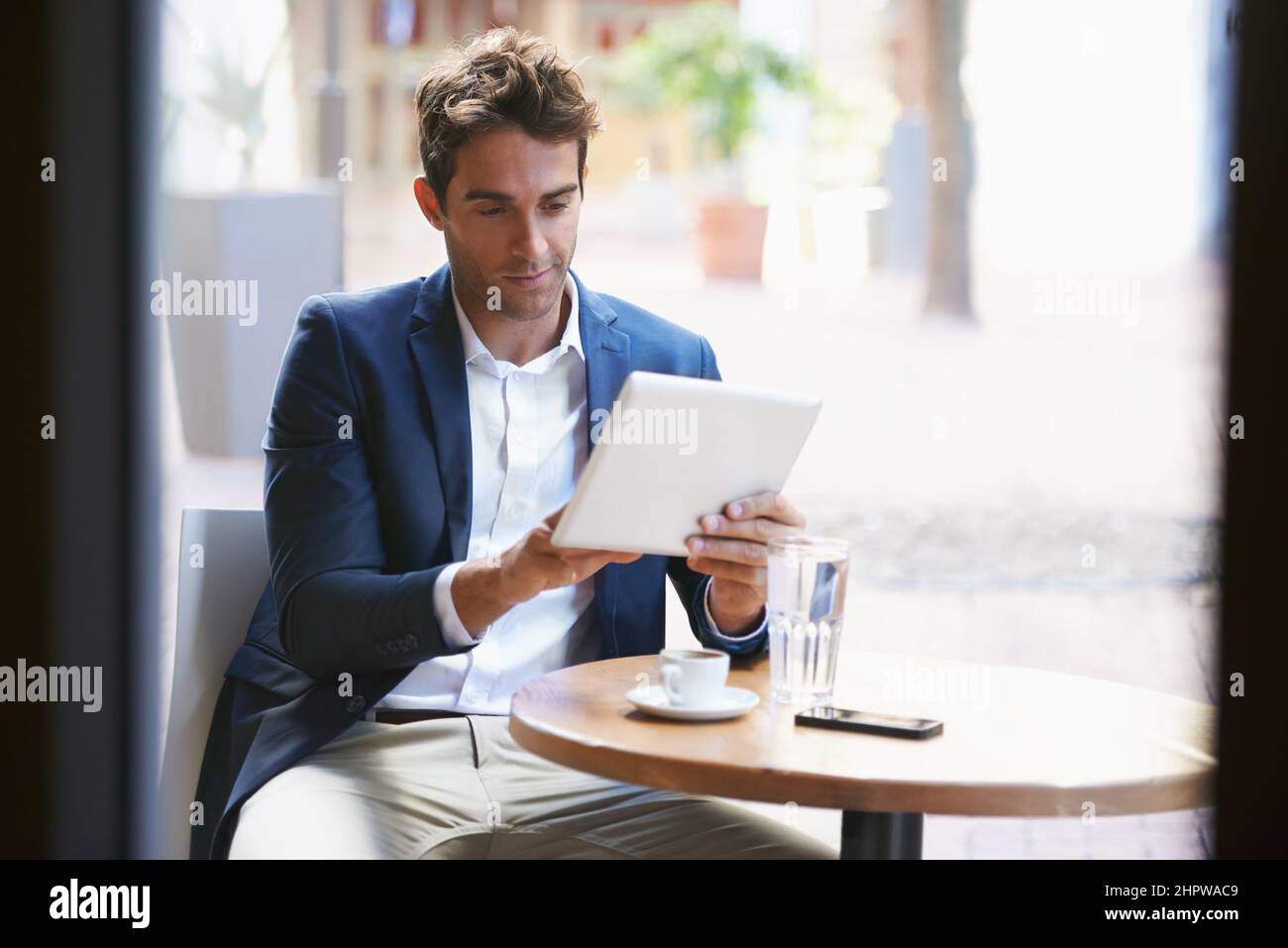 Holt seine Kaffeepause ein. Aufnahme eines jungen Geschäftsmannes, der eine Tasse Kaffee genießt, während er ein digitales Tablet benutzt. Stockfoto