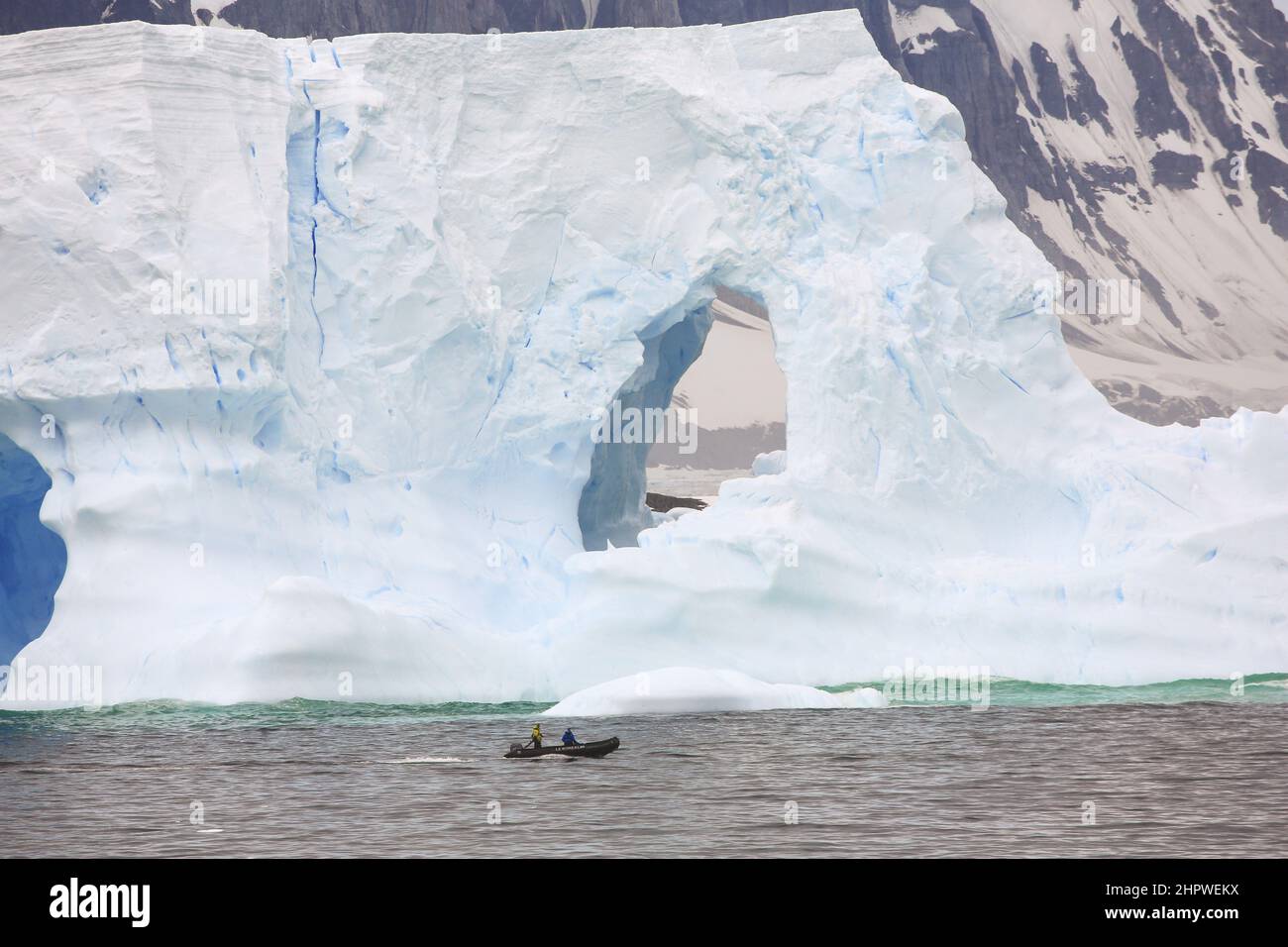 Zwei Crew in einem Tierkreisboot vom Le Boreal-Kreuzschiff passieren einen riesigen Eisberg im Südatlantik, südwestlich der Petermann-Insel, Antarktis. Stockfoto