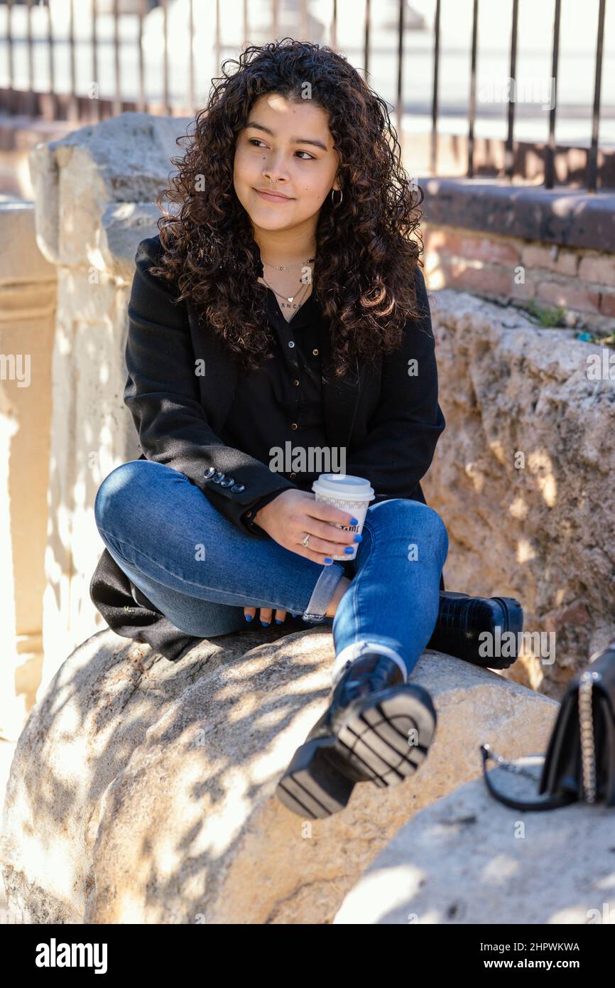 Vertikale Aufnahme einer hispanischen Frau mit lockigen Haaren, die in