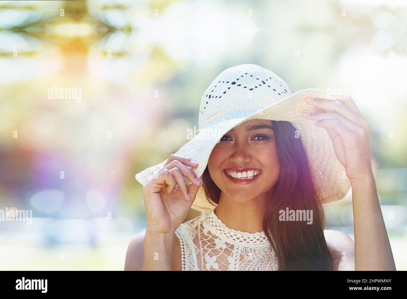Schützt meine Haut vor der Sommersonne. Eine glückliche junge Frau, die im Park steht und einen Sonnenhut trägt. Stockfoto