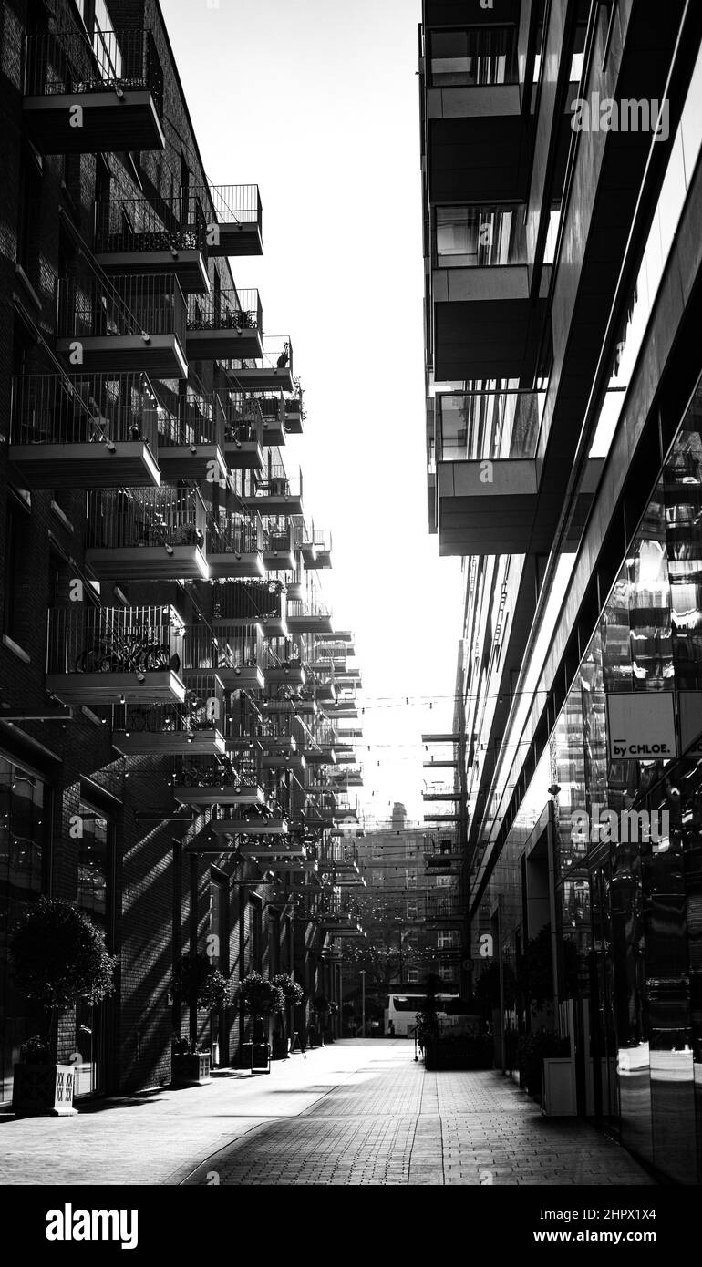 Graustufenaufnahme von Sonnenstrahlen, die eine Gasse zwischen zwei Gebäuden in London erhellen Stockfoto