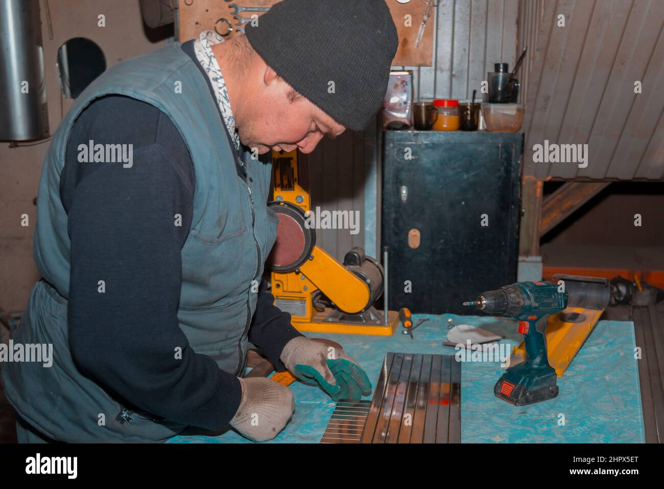 Nahaufnahme eines männlichen Arbeiters am Arbeitsplatz in einem schwarzen Strickmütze und einer ärmellosen Jacke Stockfoto